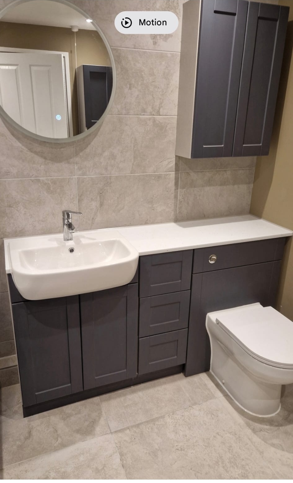 Grey vanity unit with white countertop and round illuminated mirror, bathroom installation, London.