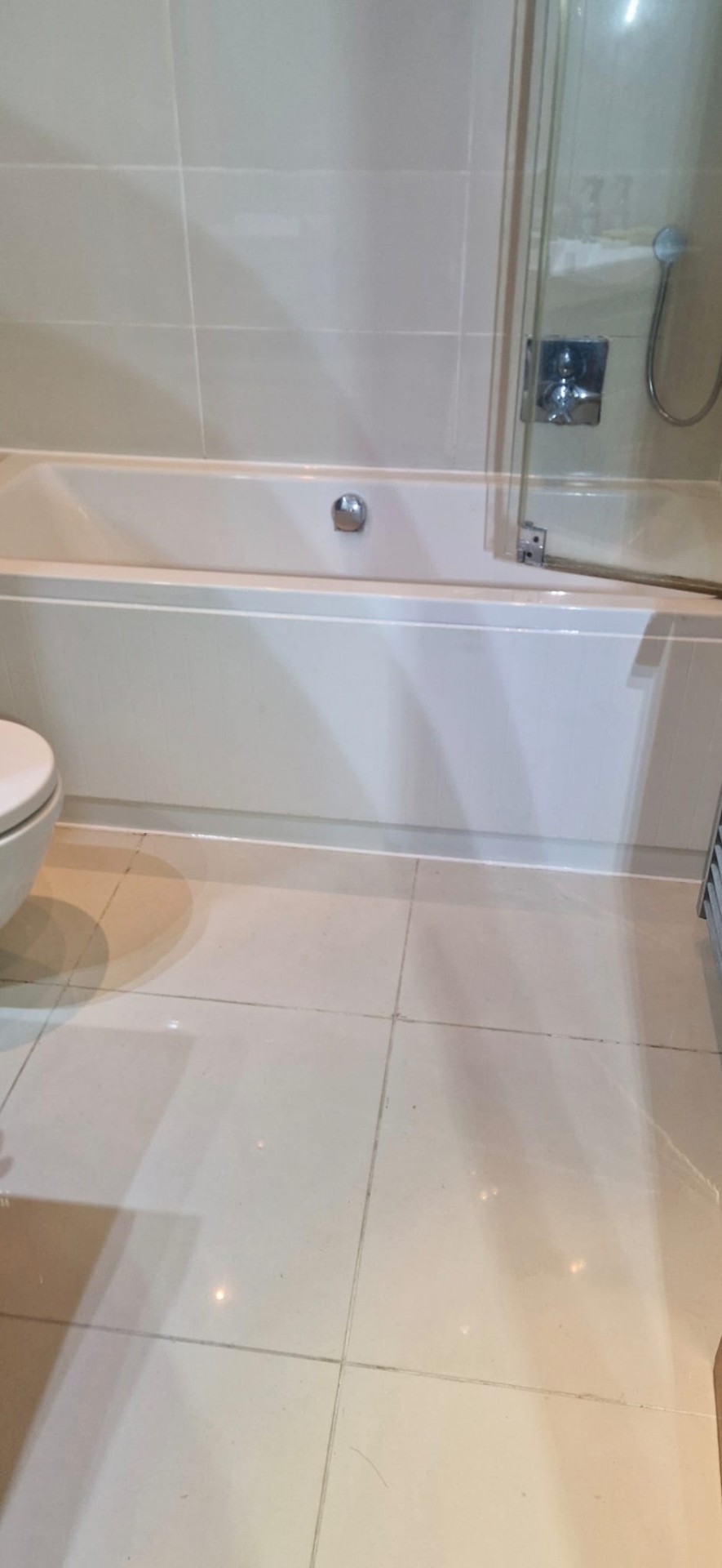 White bathtub against large beige floor tiles, bath installation by DHP London bathroom fitters.