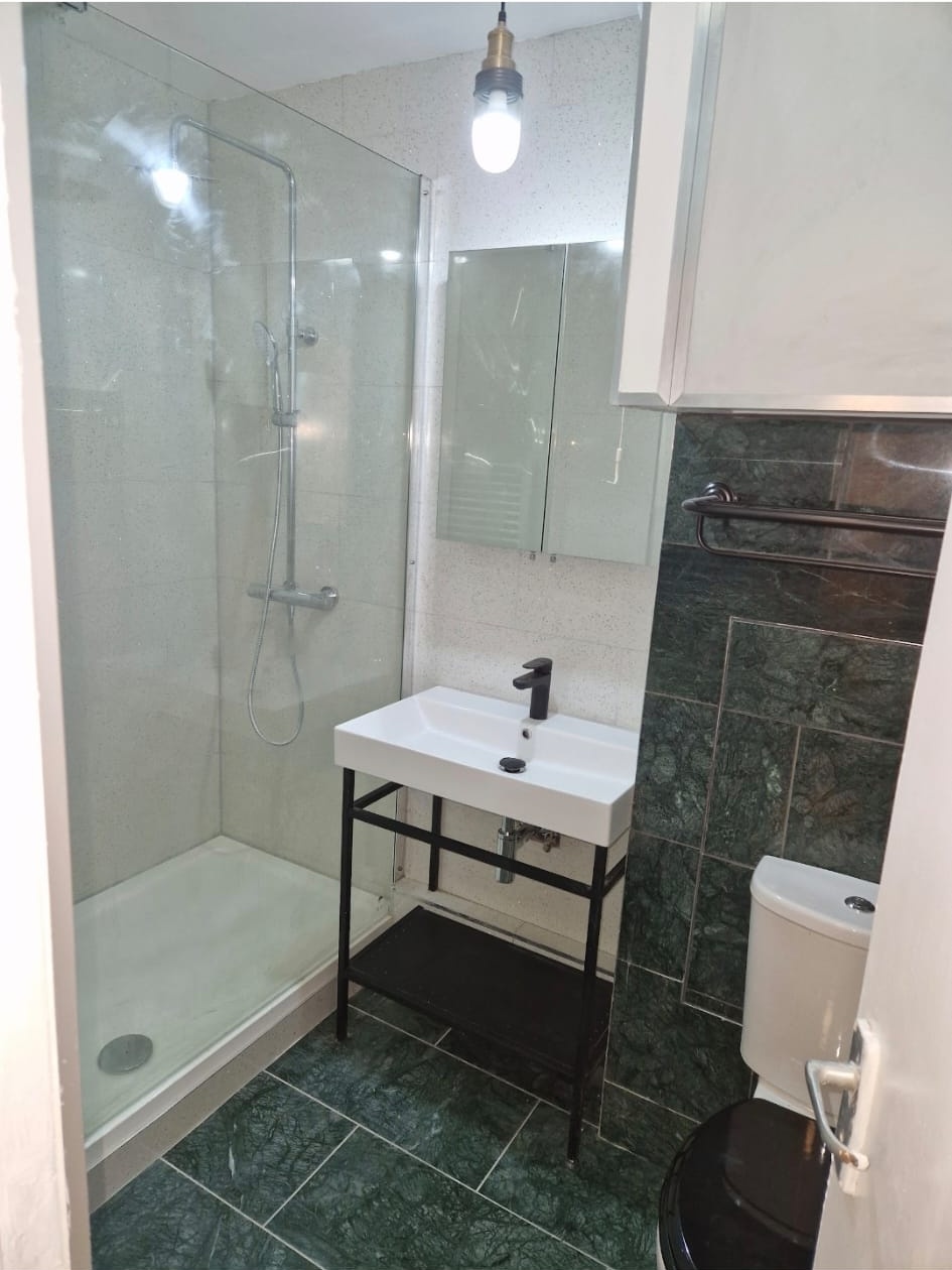 Walk-in shower with black vanity stand and green marble-effect tiles, bathroom installation.