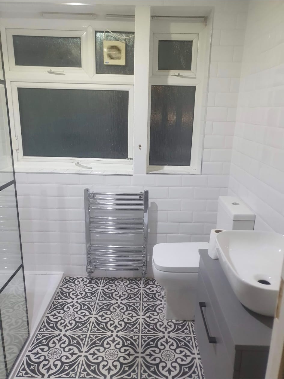 Chrome heated towel rail installed in a bathroom with white subway walls and patterned floor tiles.