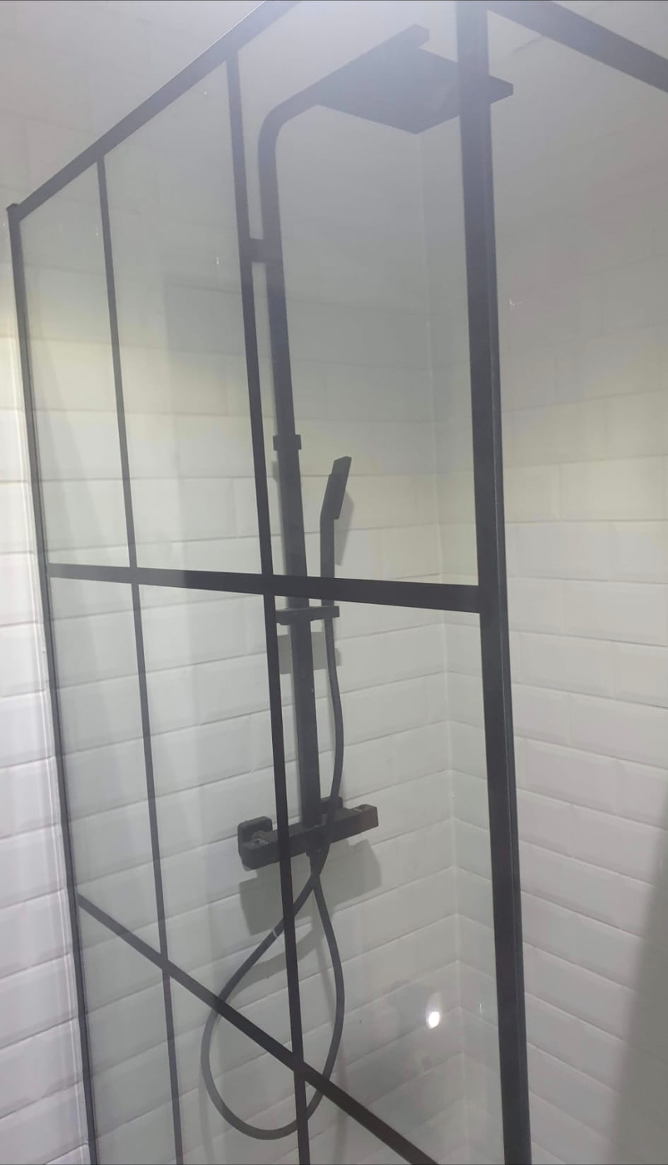 Walk-in shower with black-framed glass screen and white subway tiling by DHP London bathroom fitters.