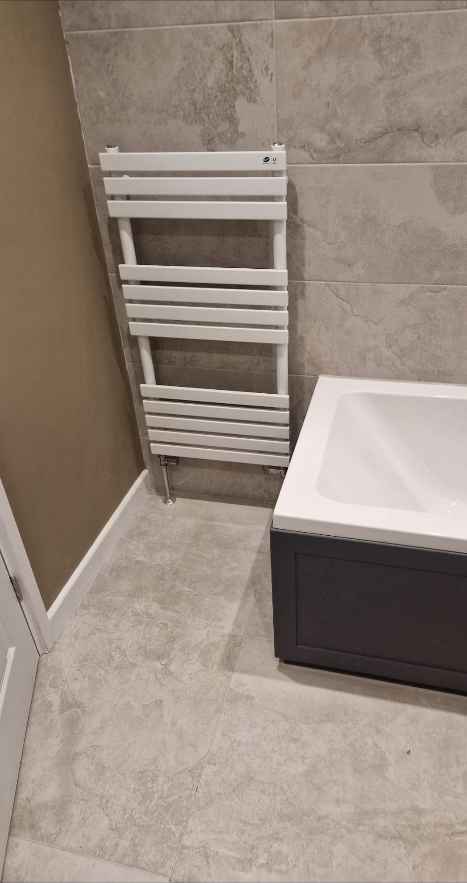 Designer heated towel rail installed next to a panelled bathtub by DHP London.