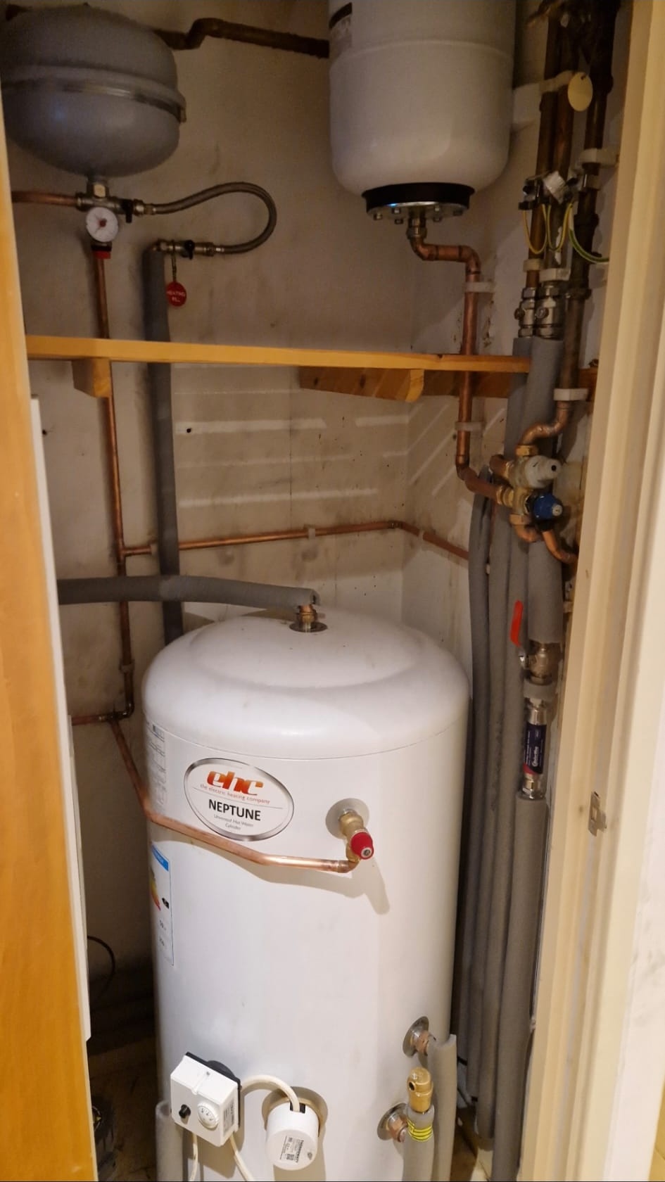 Vertical unvented hot water cylinder installation in an airing cupboard with insulated pipework.