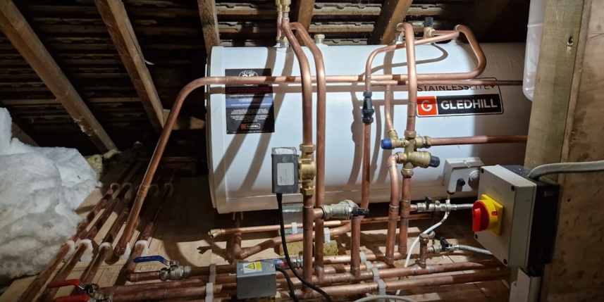 Horizontal unvented hot water cylinder installed in a loft space with copper pipework.