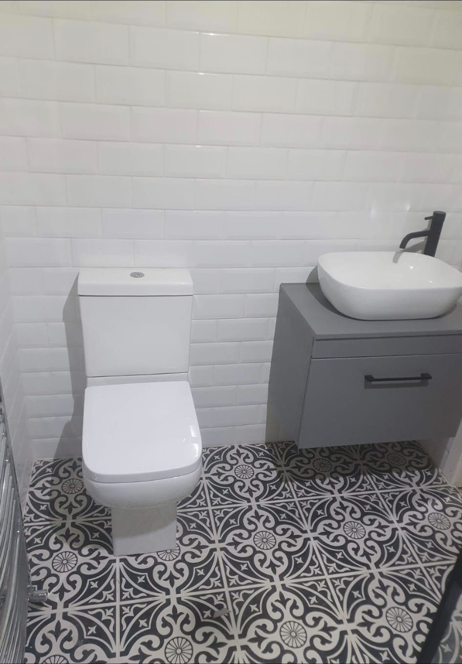 Modern toilet and grey vanity with vessel sink on patterned floor tiles, bathroom installation, London.