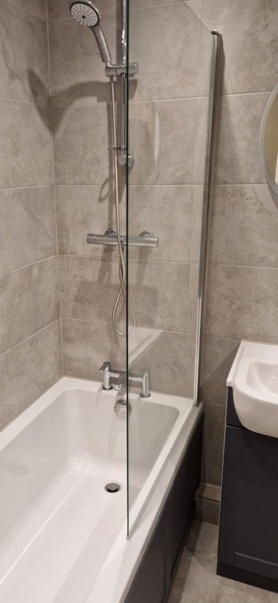White bathtub with chrome mixer taps and clear glass shower screen, bathroom installation.